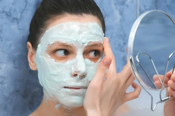 A nő alginát maszkot visel a fürdőkádban, habszivaccsal a kis tükröt nézi.. — Stock Fotó