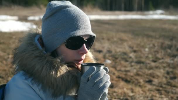 Portrait young woman in hat, sun glasses and fur jacket drinking tea on nature. — Stock Video