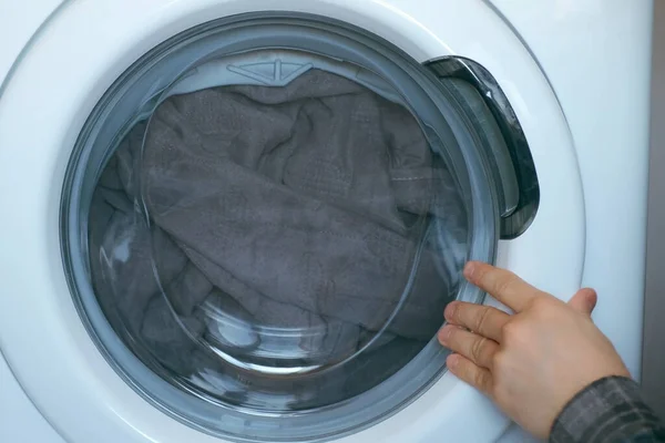 Çamaşır makinesini yatak örtüsüyle dolduran, evde çamaşır yıkayan insanlar.. — Stok fotoğraf