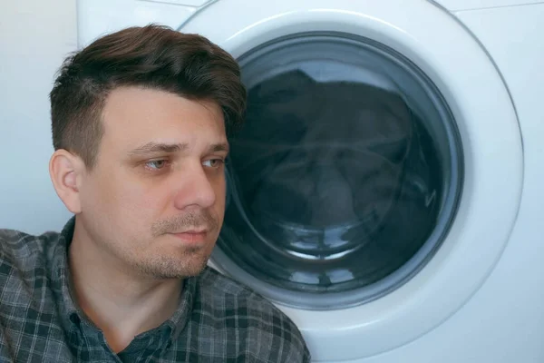 Moe man wacht op de wasmachine met grijze sprei erin. — Stockfoto