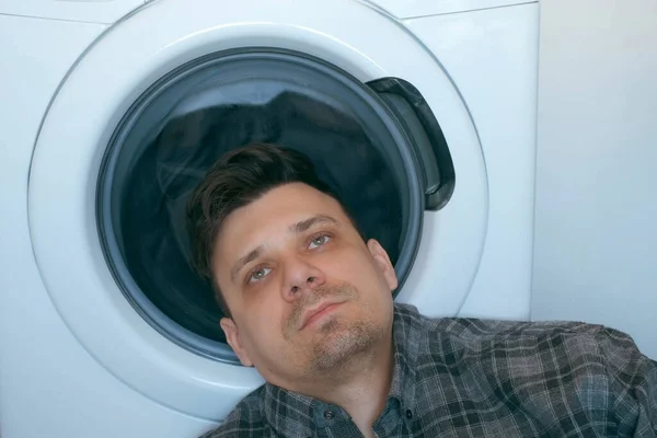 Уставший человек ждет стиральную машину с серым покрывалом внутри. — стоковое фото