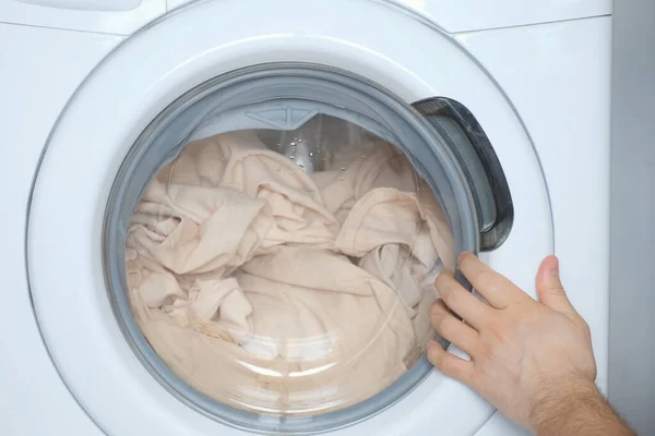 Çamaşır makinesini bej çarşaflarla dolduran, evde çamaşır yıkayan insanlar.. — Stok fotoğraf
