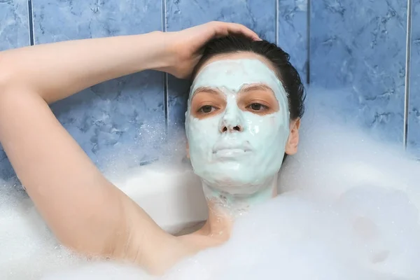 Young woman with alginate mask relaxing lying in bathroom with foam at home. — Stock Photo, Image