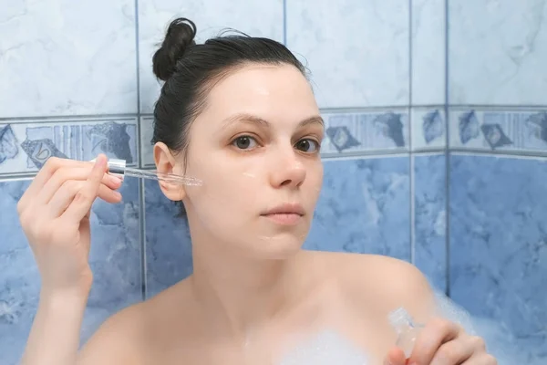 Mujer joven está aplicando ácido hialurónico en la piel de la cara tomando un baño con espuma. — Foto de Stock