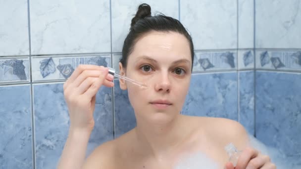 Mujer joven está aplicando ácido hialurónico en la piel de la cara tomando un baño con espuma. — Vídeos de Stock