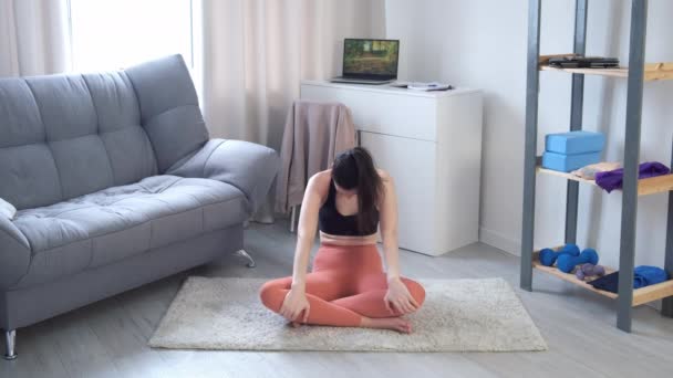 Mujer joven está haciendo inclinación lenta hacia adelante en el yoga sentado en la estera en casa. — Vídeo de stock