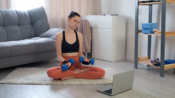 Jonge vrouw doet biceps oefening met behulp van halters thuis training online. — Stockvideo