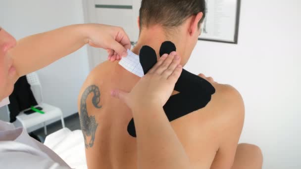 Physiotherapist applys kinesio tapes to man patients neck shoulder in clinic. — Stock Video