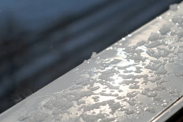 Wiosenne krople i topniejący śnieg na parapecie za oknem, zbliżenie. — Zdjęcie stockowe