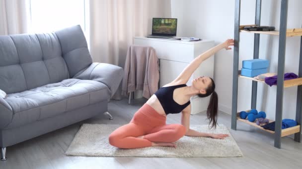 Kobieta robi ćwiczenia rozciągające jogę siedząc na dywanie w domu, widok z przodu. — Wideo stockowe