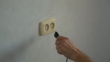Bir adamın eli, bir elektrik aletinin çatalını prize çevirir..