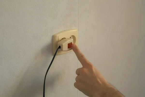 Mans Hand schaltet den Stecker in eine Steckdose und drückt den roten Knopf. — Stockfoto