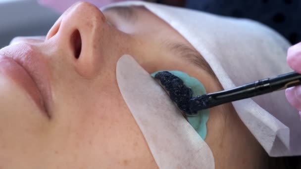 Косметолог наносить чорну фарбу на жіночі вії, ламінуючи процедуру вії . — стокове відео