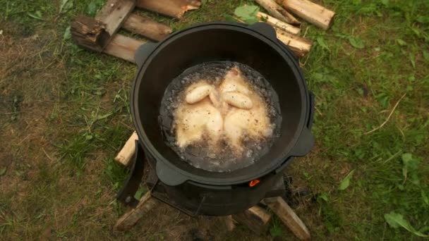 Menggoreng ayam di cazan hitam dengan minyak mendidih di kompor pembakaran kayu di alam. — Stok Video