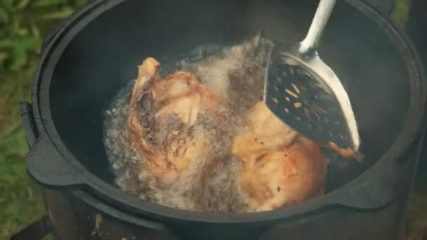 Steka kyckling i svart kazan med kokande olja i vedeldad spis på naturen. — Stockvideo