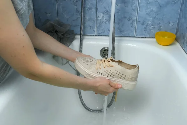 Vrouw is wassen sport schoenen in badkamer door handen, close-up handen. — Stockfoto