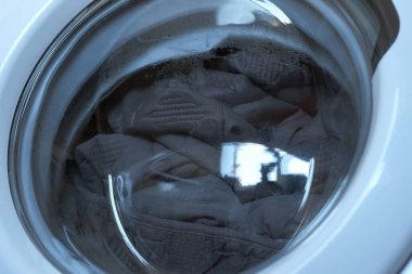 İçinde gri yatak örtüsü olan çamaşır makinesi çalışıyor, evde çamaşır yıkılıyor..