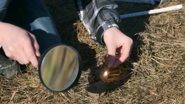草に火をつけようとする虫眼鏡をかけた少年の手. — ストック動画