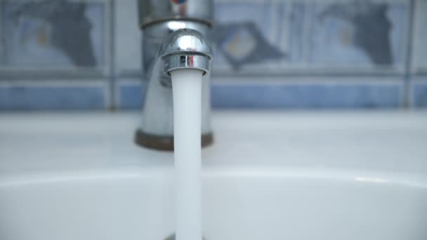 Clear water is pouring from shiny faucel into the sink in bathroom, closeup. — Stock Video