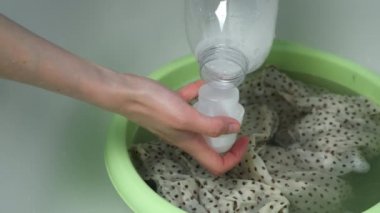 Kadın, narin kumaştan elbiseyi leğende durulama makinesinde elleriyle yıkıyor..