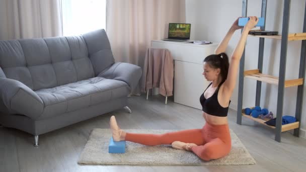 Młoda kobieta ćwiczy jogę robiąc pochylenia w pozycji siedzącej do przodu zakręt w domu. — Wideo stockowe