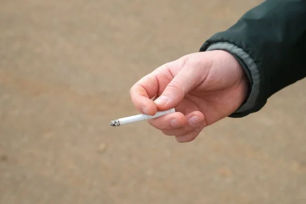 Mano de hombre con un cigarrillo humeante fumar un mal hábito. — Foto de Stock