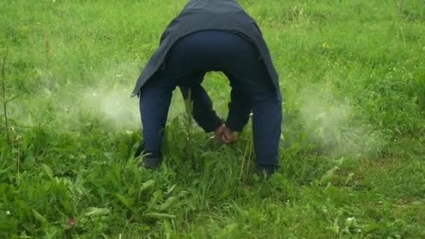 Ein Mann putzt einen Grillrost auf dem Rasen in der Natur und bereitet sich auf das Kochen vor. — Stockvideo