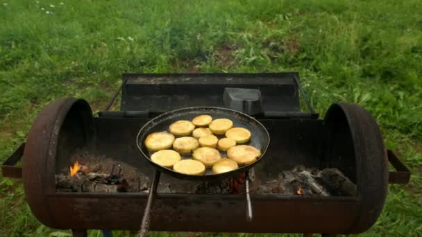 Кусочки цуккини жарят на сковороде с маслом на углях в гриле на природе. — стоковое видео