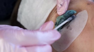 Kirpik kaplama prosedürüne kirpiklerini siyah boyayla silen bir güzellik uzmanı..