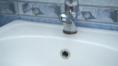 Musluktan damlayan su banyodaki beyaz lavaboya akıyor, yakın çekim manzarası..