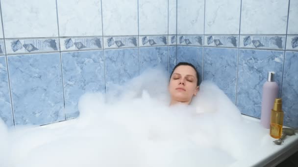 Young woman with closed eyes relaxing lying in bath with foam after busy day. — Stock Video