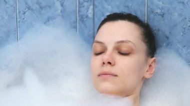 Kapalı gözlü genç bir kadın. Yoğun bir günden sonra banyoda köpükle dinleniyor..