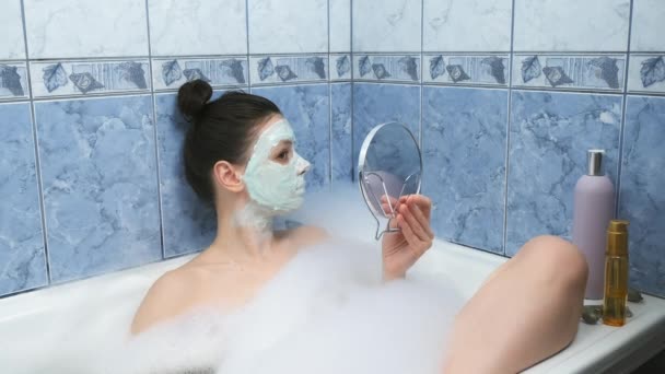 Woman is applying alginate mask in bathr with foam looking at small mirror. — Stock Video