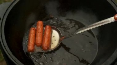 Adam kazanın içinden spatula kullanarak lezzetli sosisler çıkarıyor, yakın plan görüntü..