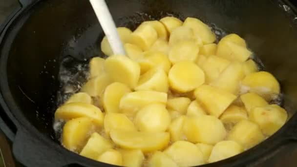 Miscelazione di patate fritte con spatola, cottura in calderone in olio sul fuoco naturale. — Video Stock