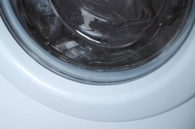 Çamaşır makinesi gri yatak örtüsünü yıkar, pencereyi kapatır..