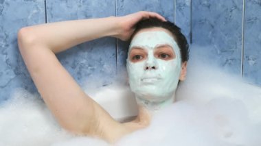 Aljinat maskeli genç bir kadın banyoda köpükle dinleniyor..