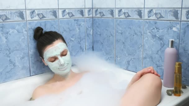 年轻女子戴着海藻酸钠面罩，悠闲地躺在浴室里，满屋子泡沫. — 图库视频影像