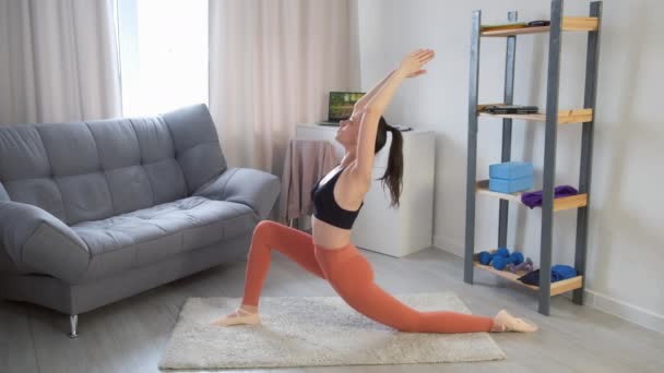 Mujer joven practica pose guerrera I virabhadasana haciendo yoga en casa. — Vídeo de stock