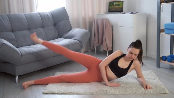 Sportieve jonge vrouw doet oefeningen rijzen been omhoog liggend op kant op tapijt. — Stockvideo