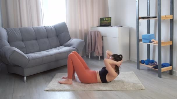 Mujer joven en ropa deportiva está haciendo ejercicios abdominales flexionar las piernas en la alfombra en casa. — Vídeo de stock