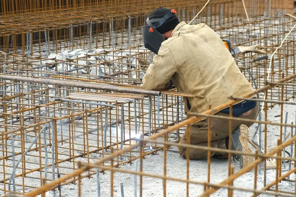 Man lasser is lassen metalen frame voor betonnen fundering van het gebouw. — Stockfoto