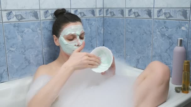 Mujer joven está aplicando máscara de alginato acostado en el baño con espuma en casa. — Vídeo de stock