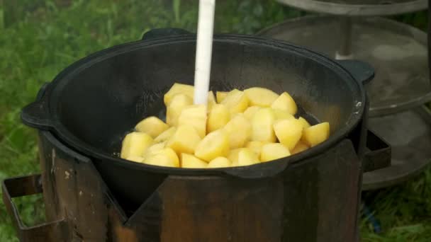 Miscelazione di patate fritte con spatola, cottura in calderone in olio sul fuoco naturale. — Video Stock