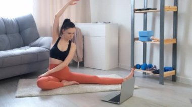Kadın evde diz üstü bilgisayara bakarak yan eğik egzersizler yapıyor..