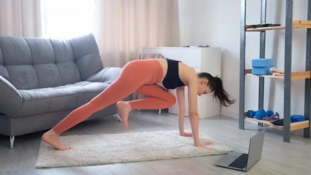 Jovem mulher fazendo prancha flexionando pernas exercício em dinâmica em casa, vista lateral. — Vídeo de Stock