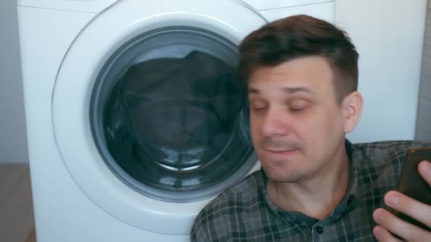 Man wacht op de wasmachine met bedsprei en praten op smartphone. — Stockvideo