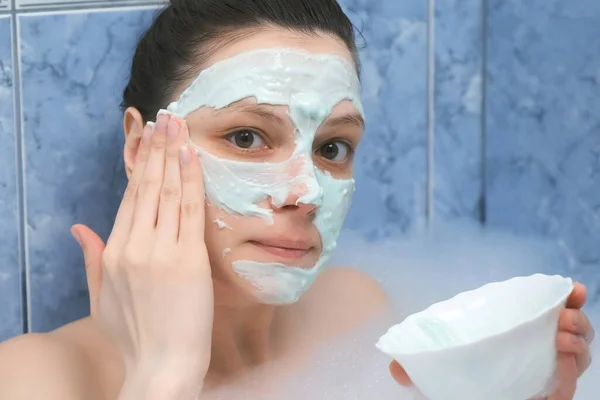 Young woman is applying alginate mask lying in bathroom with foam at home. — Stock Photo, Image