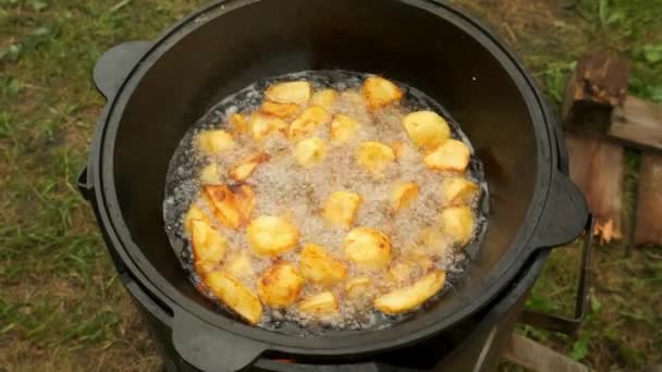 Ruddy välsmakande potatis steker i kittel i olja på naturen i brand, närbild. — Stockvideo