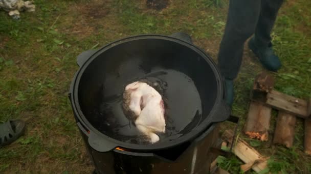 Muži dávají kuře do černého cazanu s vařícím olejem na smažení. — Stock video